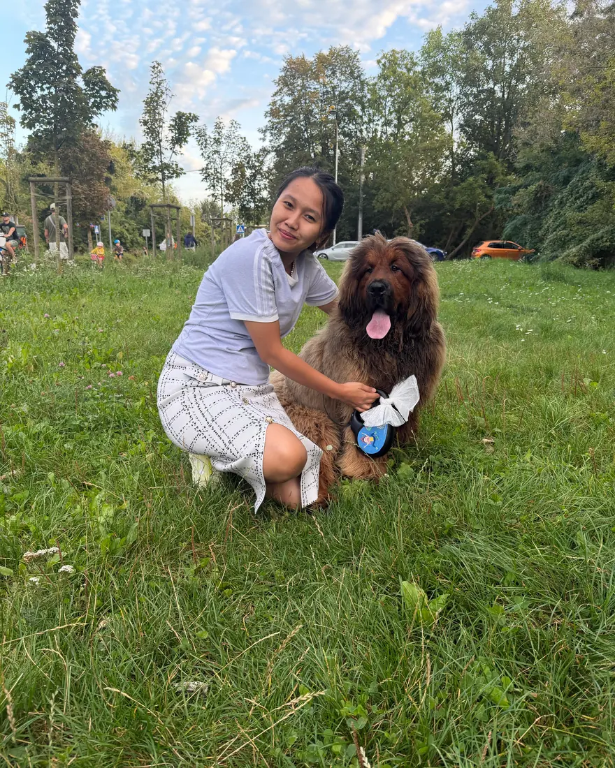 Escort crouching beside a long-haired dog on the grass